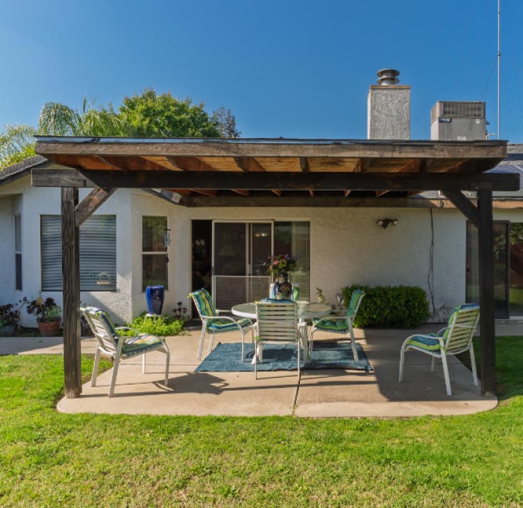 The peaceful outdoor patio at Guardian Angel Home Care features a glass table with floral arrangements and comfortable seating under a shaded pergola, offering a serene environment for residents to relax.