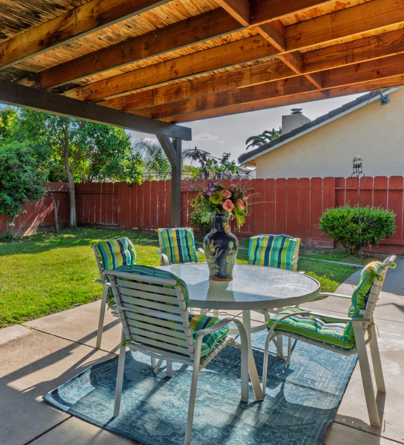 The peaceful outdoor patio at Guardian Angel Home Care features a glass table with floral arrangements and comfortable seating under a shaded pergola, offering a serene environment for residents to relax.