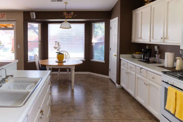 the bright and clean residential kitchen and dining area at Guardian Angel Home Care, featuring a wooden table set by large bay windows. The home-like setting is designed to offer a familiar, non-institutional atmosphere for seniors in Atwater, CA.