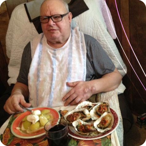 Lidia's father, who became disabled shortly after the facility opened and served as the very first client at Guardian Angel Home Care. He is shown enjoying a specialized, home-cooked meal, illustrating the personal roots of the company's caregiving standards.